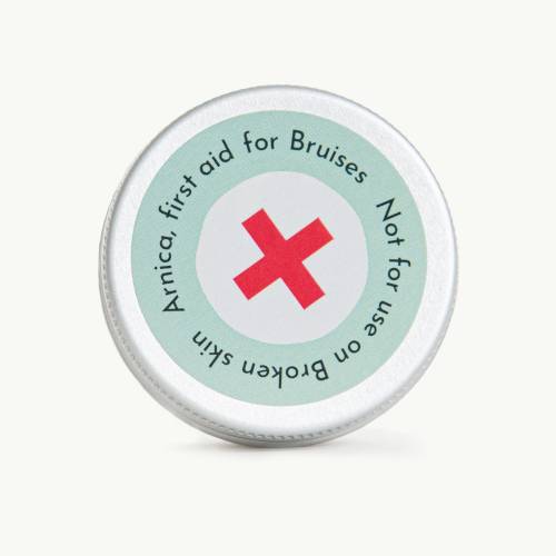 Small tin of Arnica salve, with a red cross on the label on a soft grey background